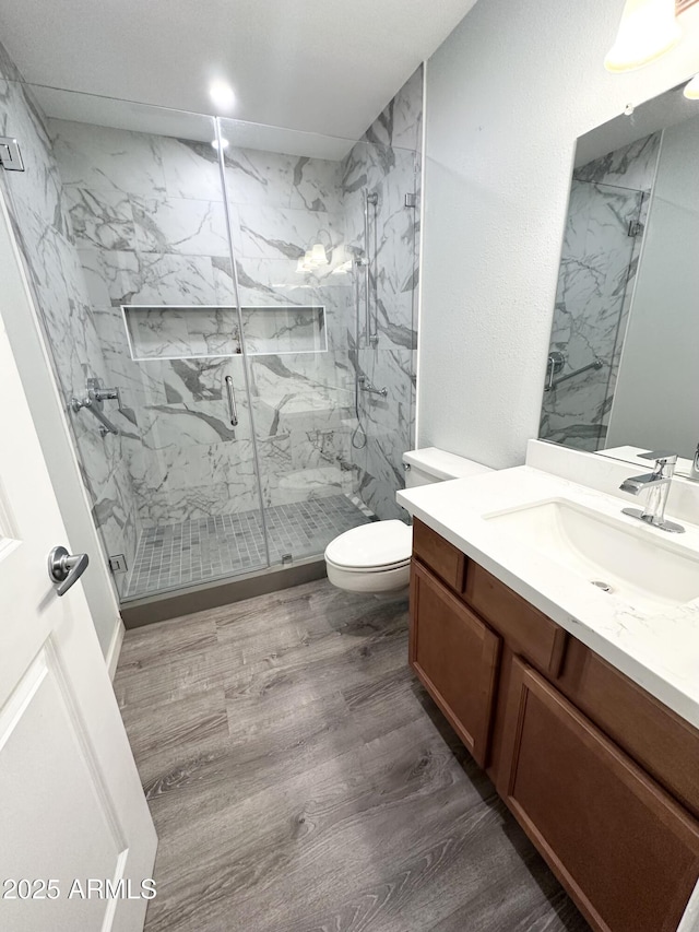 full bath with toilet, a marble finish shower, wood finished floors, and vanity