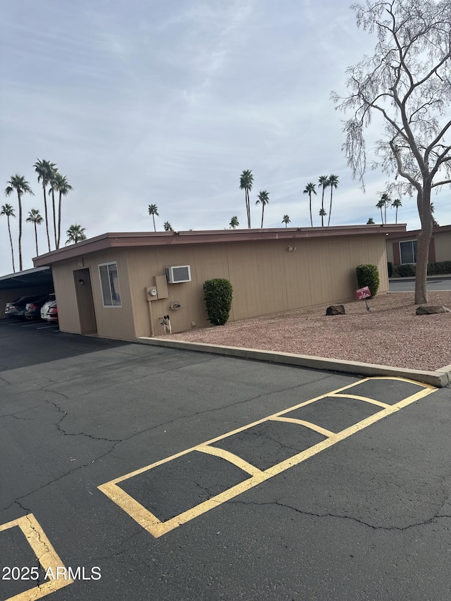 view of front of property with a wall mounted AC and covered and uncovered parking