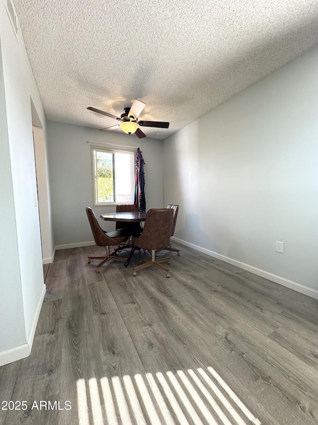 unfurnished dining area with ceiling fan, a textured ceiling, baseboards, and wood finished floors