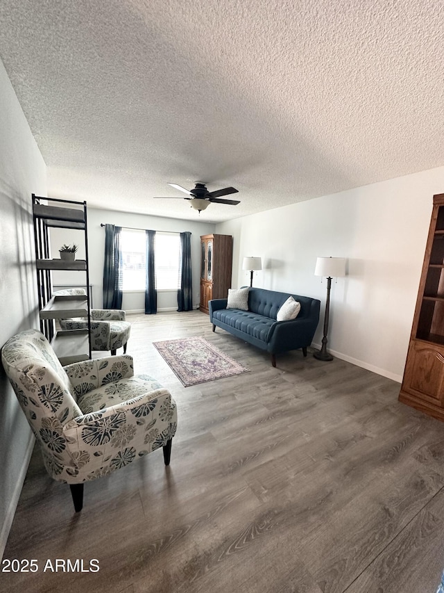 living area with baseboards, a textured ceiling, a ceiling fan, and wood finished floors