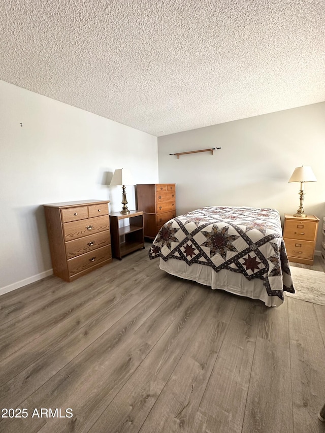 bedroom with a textured ceiling, baseboards, and wood finished floors