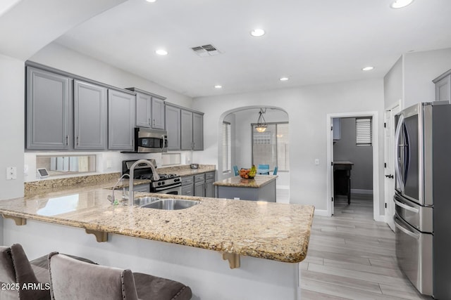 kitchen featuring visible vents, a peninsula, light stone countertops, stainless steel appliances, and gray cabinetry