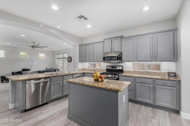 kitchen featuring visible vents, a peninsula, gray cabinets, stainless steel appliances, and a sink