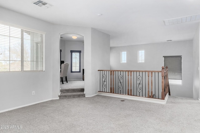 carpeted empty room with arched walkways, visible vents, and baseboards