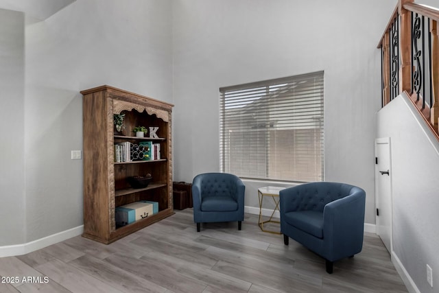 living area featuring light wood-style floors, baseboards, and a high ceiling