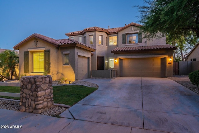 mediterranean / spanish-style house with a tile roof, stucco siding, fence, a garage, and driveway