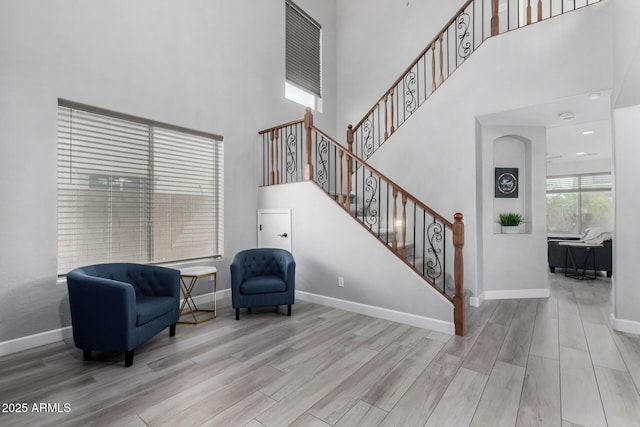 sitting room with baseboards, a high ceiling, stairs, and light wood-style floors