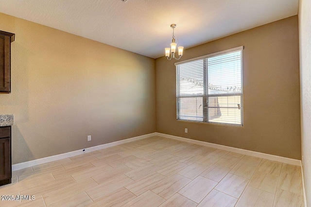 spare room featuring a chandelier and baseboards