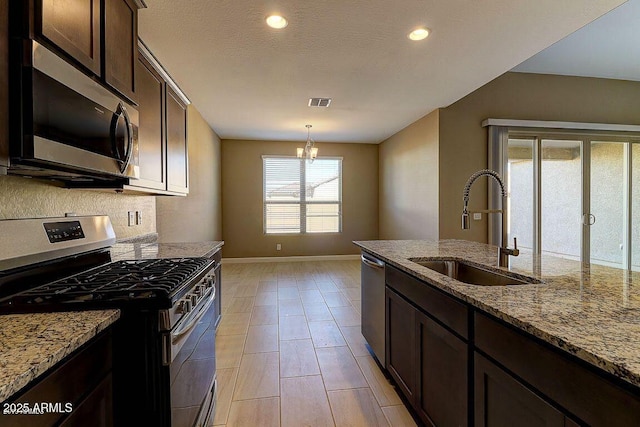 kitchen with stainless steel appliances, dark brown cabinets, a sink, and light stone countertops