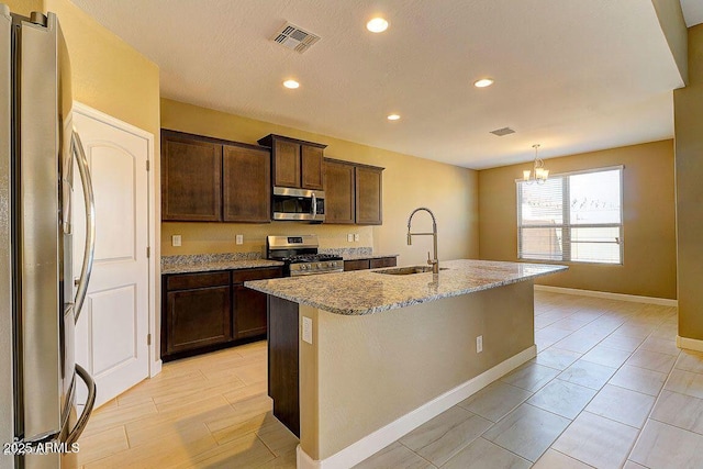 kitchen featuring light stone counters, a kitchen island with sink, stainless steel appliances, a sink, and visible vents