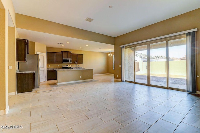 kitchen with a sink, visible vents, open floor plan, dark brown cabinets, and appliances with stainless steel finishes