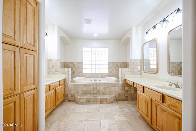 bathroom with a relaxing tiled tub, vanity, and tile patterned flooring