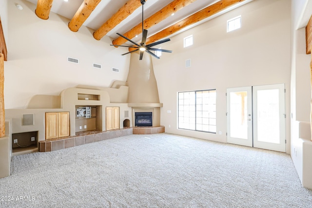 unfurnished living room with ceiling fan, carpet, a fireplace, french doors, and beamed ceiling