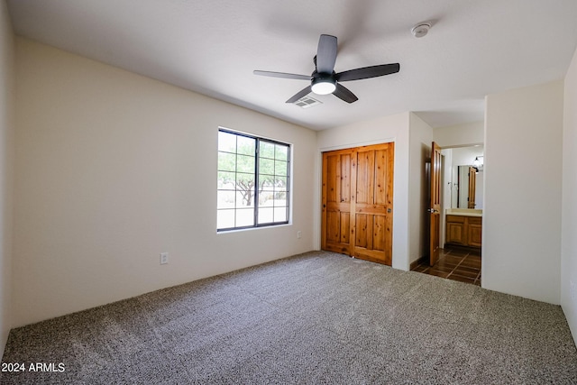 unfurnished bedroom featuring dark carpet, a closet, ceiling fan, and ensuite bathroom