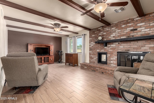 living room with light wood-style floors, beamed ceiling, ceiling fan, a fireplace, and visible vents