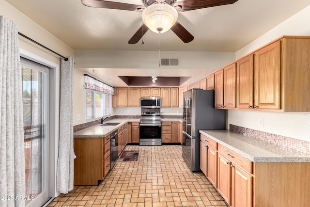 kitchen featuring visible vents, a sink, appliances with stainless steel finishes, a ceiling fan, and brick floor