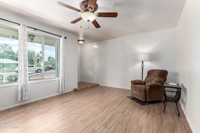living area with baseboards, light wood-type flooring, and a ceiling fan