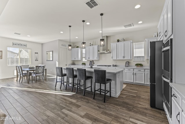 kitchen with visible vents, a breakfast bar area, wall chimney exhaust hood, and light countertops