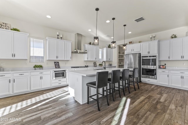 kitchen with visible vents, appliances with stainless steel finishes, white cabinetry, and wall chimney range hood