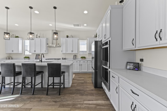 kitchen with a breakfast bar, white cabinets, wall chimney exhaust hood, and visible vents