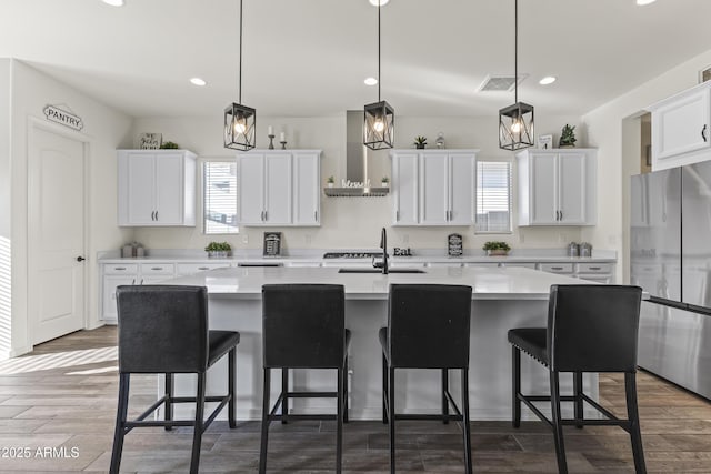 kitchen with wall chimney exhaust hood, a healthy amount of sunlight, visible vents, and freestanding refrigerator