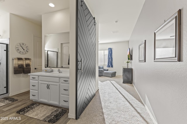 hall featuring a barn door, light wood-style floors, baseboards, and visible vents