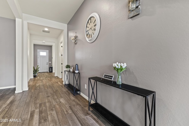 hall with visible vents, baseboards, and wood finished floors