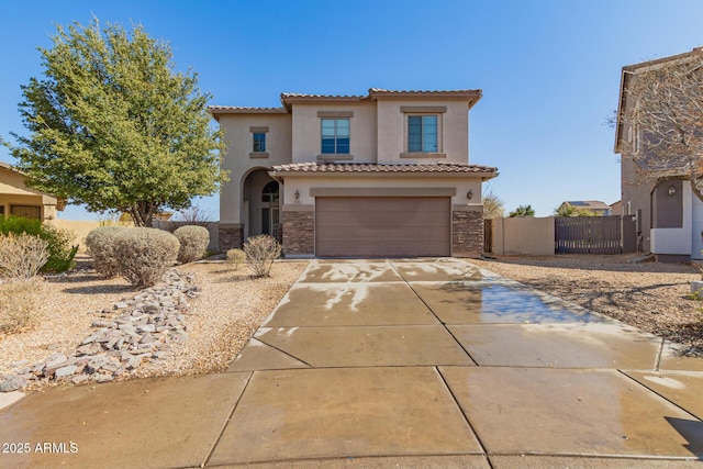 mediterranean / spanish house with concrete driveway, a tile roof, stucco siding, stone siding, and a gate