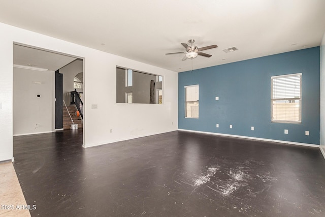 spare room featuring visible vents, finished concrete flooring, baseboards, ceiling fan, and stairway