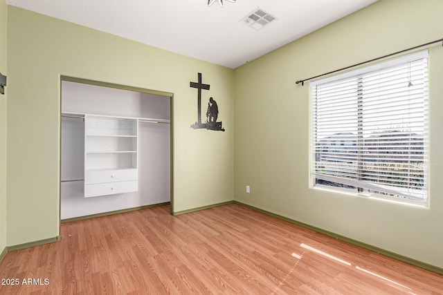 unfurnished bedroom featuring wood finished floors, visible vents, a closet, and baseboards