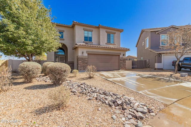 mediterranean / spanish-style house with stucco siding, driveway, a tile roof, stone siding, and an attached garage