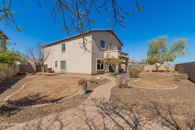 back of house featuring stucco siding, a balcony, and a fenced backyard