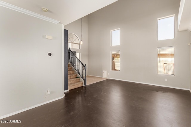 unfurnished living room with stairway, a healthy amount of sunlight, and baseboards