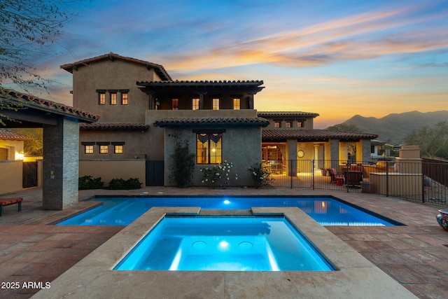 back house at dusk with a pool with hot tub, a mountain view, a patio area, and a balcony