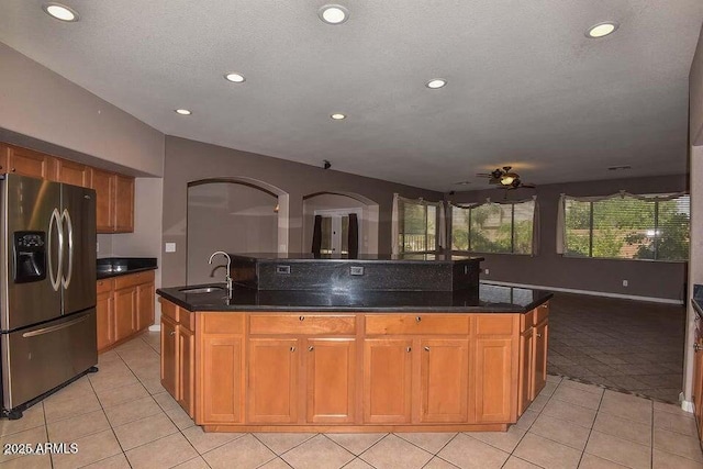 kitchen with ceiling fan, light tile patterned flooring, a kitchen island with sink, a textured ceiling, and stainless steel fridge