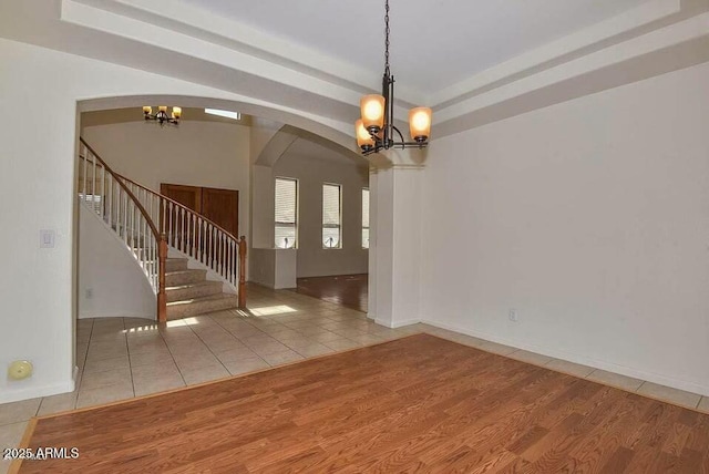 unfurnished room with light tile patterned floors, a raised ceiling, and a notable chandelier