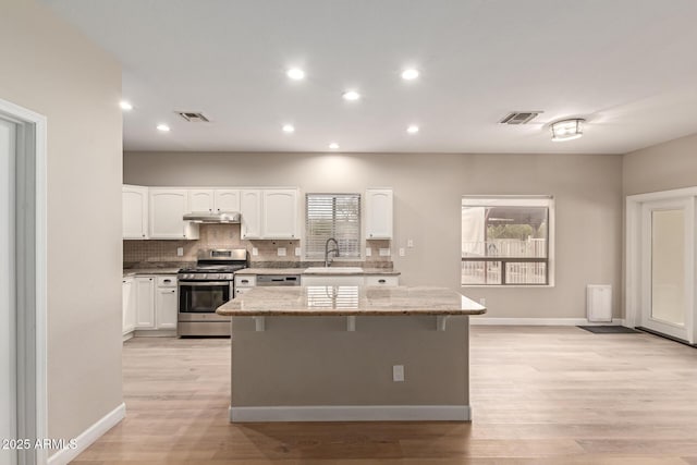 kitchen with a sink, stainless steel range with gas cooktop, visible vents, and under cabinet range hood