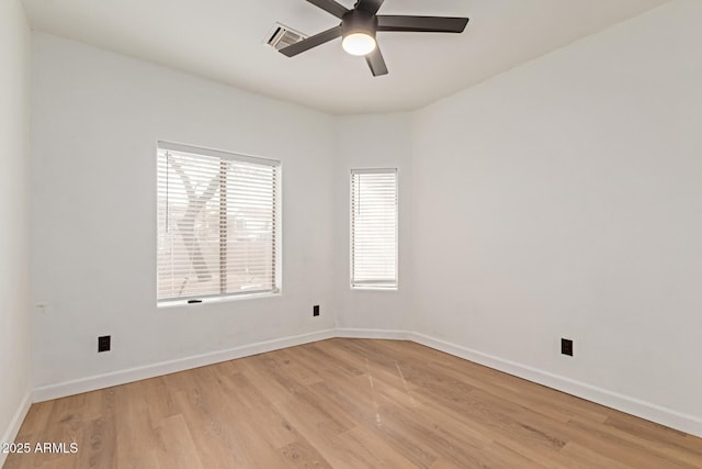 spare room featuring light wood finished floors, a ceiling fan, visible vents, and baseboards