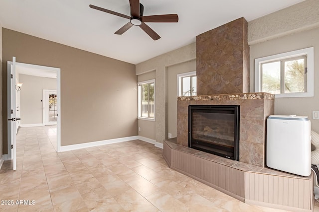 unfurnished living room with a ceiling fan, baseboards, and a tiled fireplace