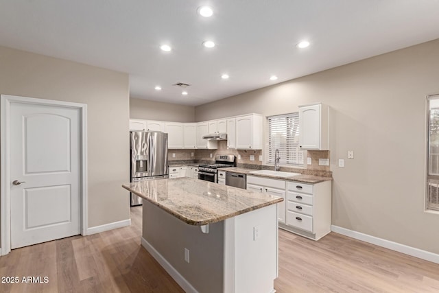 kitchen with appliances with stainless steel finishes, tasteful backsplash, a sink, and light stone countertops