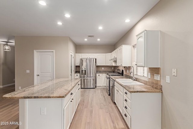 kitchen featuring appliances with stainless steel finishes, a sink, a center island, and light wood-style floors