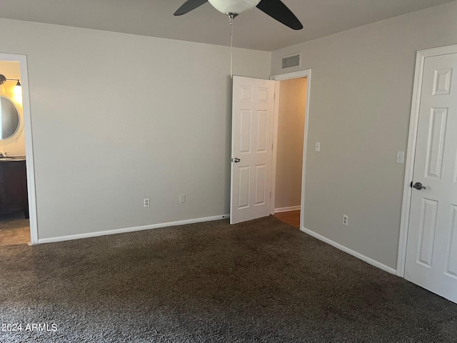 unfurnished bedroom featuring ceiling fan, ensuite bath, and dark colored carpet