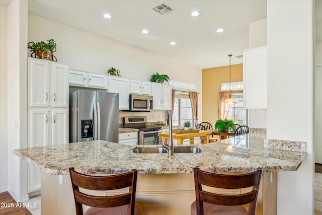 kitchen with decorative light fixtures, stainless steel appliances, kitchen peninsula, and a breakfast bar