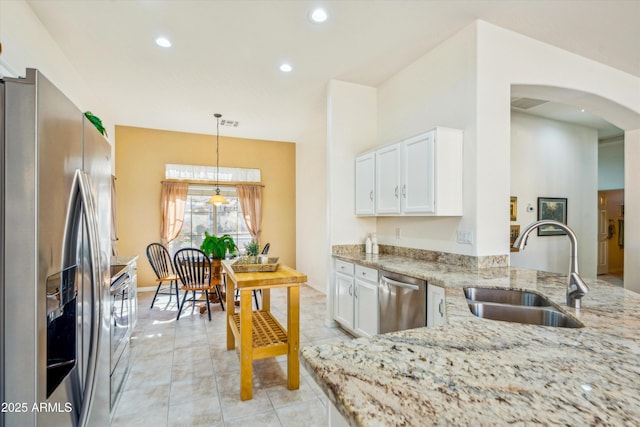 kitchen with sink, appliances with stainless steel finishes, light stone countertops, white cabinets, and decorative light fixtures