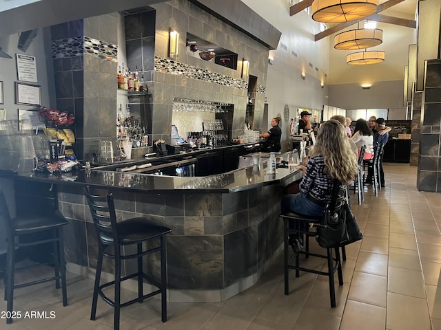 bar featuring a community bar, light tile patterned floors, decorative backsplash, and beamed ceiling