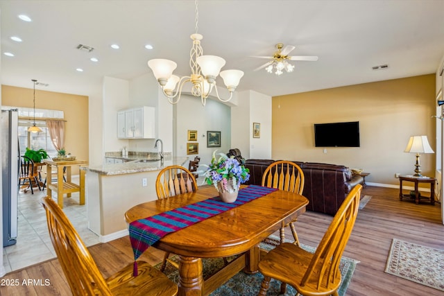 dining room with ceiling fan with notable chandelier, sink, and light wood-type flooring