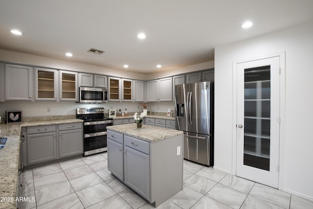 kitchen featuring light stone counters, stainless steel appliances, a kitchen island, and gray cabinetry