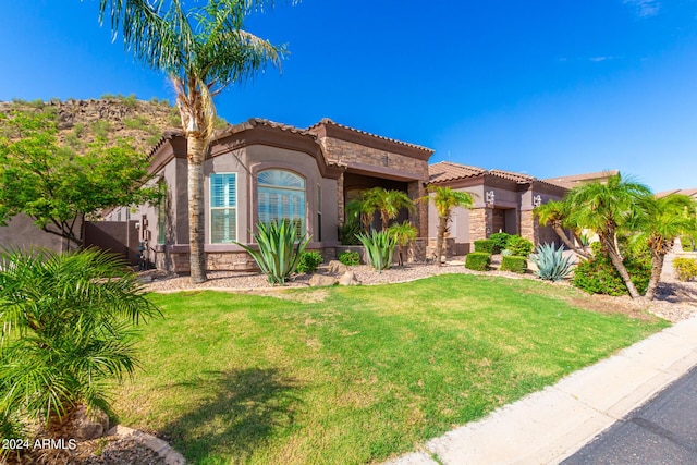 mediterranean / spanish home with stone siding, a front yard, a tiled roof, and stucco siding