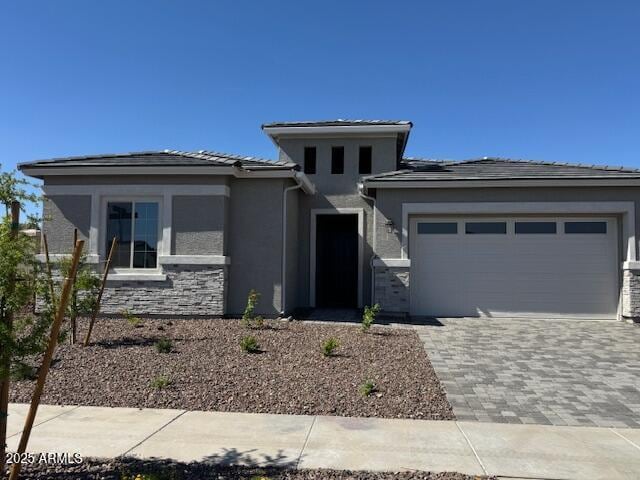 prairie-style home featuring a garage, stucco siding, decorative driveway, and stone siding