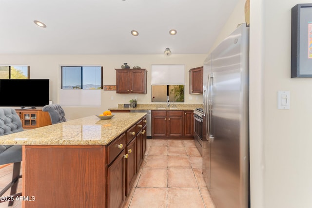 kitchen featuring sink, a breakfast bar, stainless steel appliances, a center island, and light stone countertops